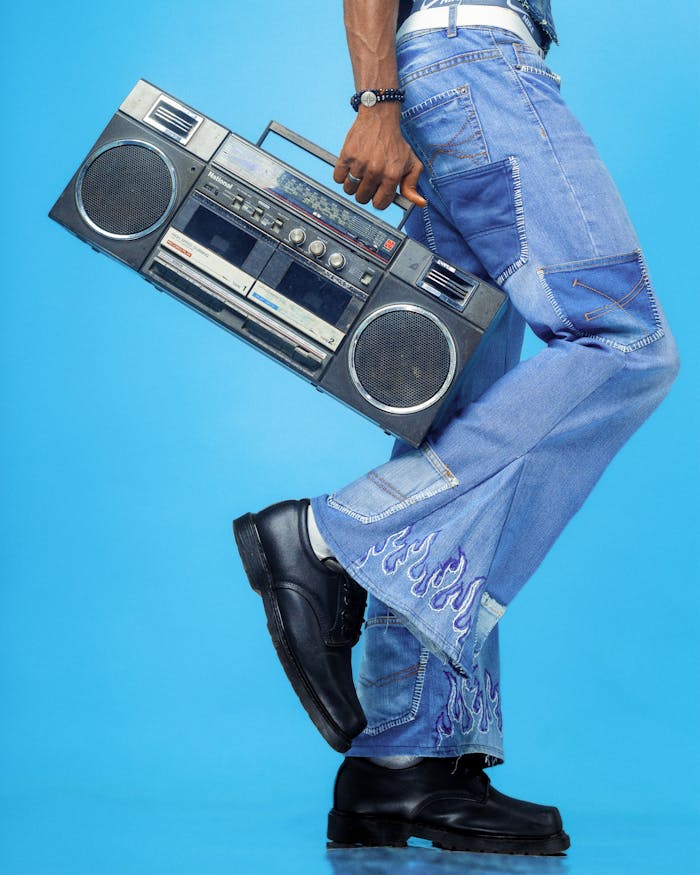 Man holding vintage boombox dressed in stylish denim on blue background.